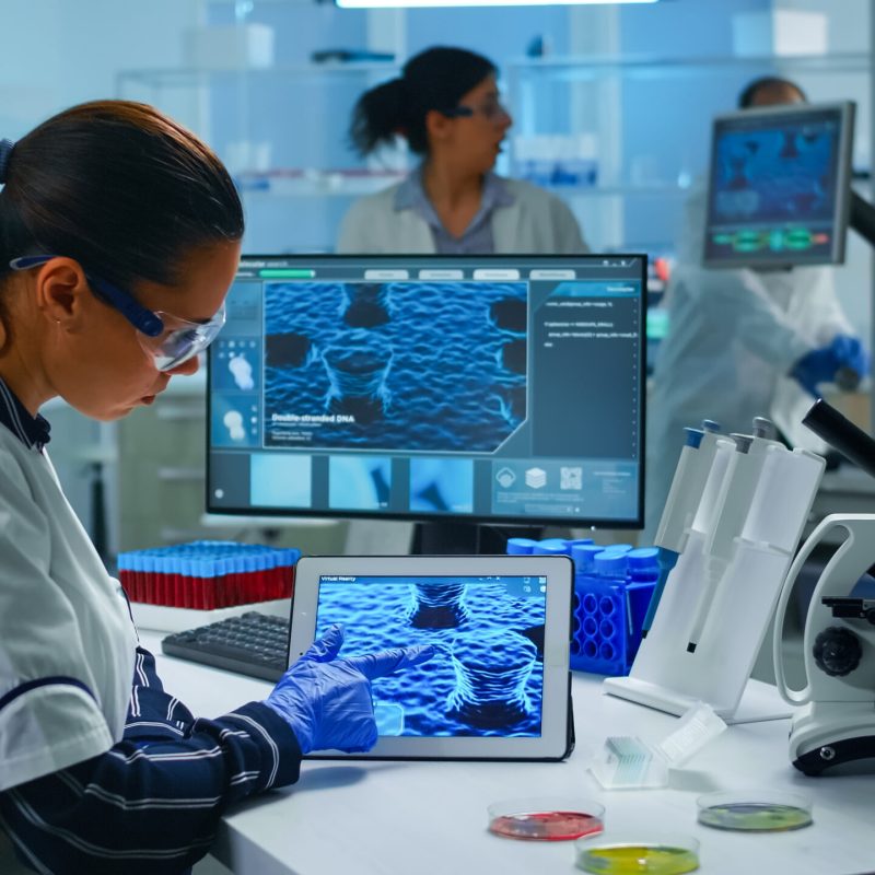 Lab technician doctor analyzing virus evolution looking on digital tablet. Team of scientists conducting vaccine development using high tech for researching treatment against covid19 pandemic.